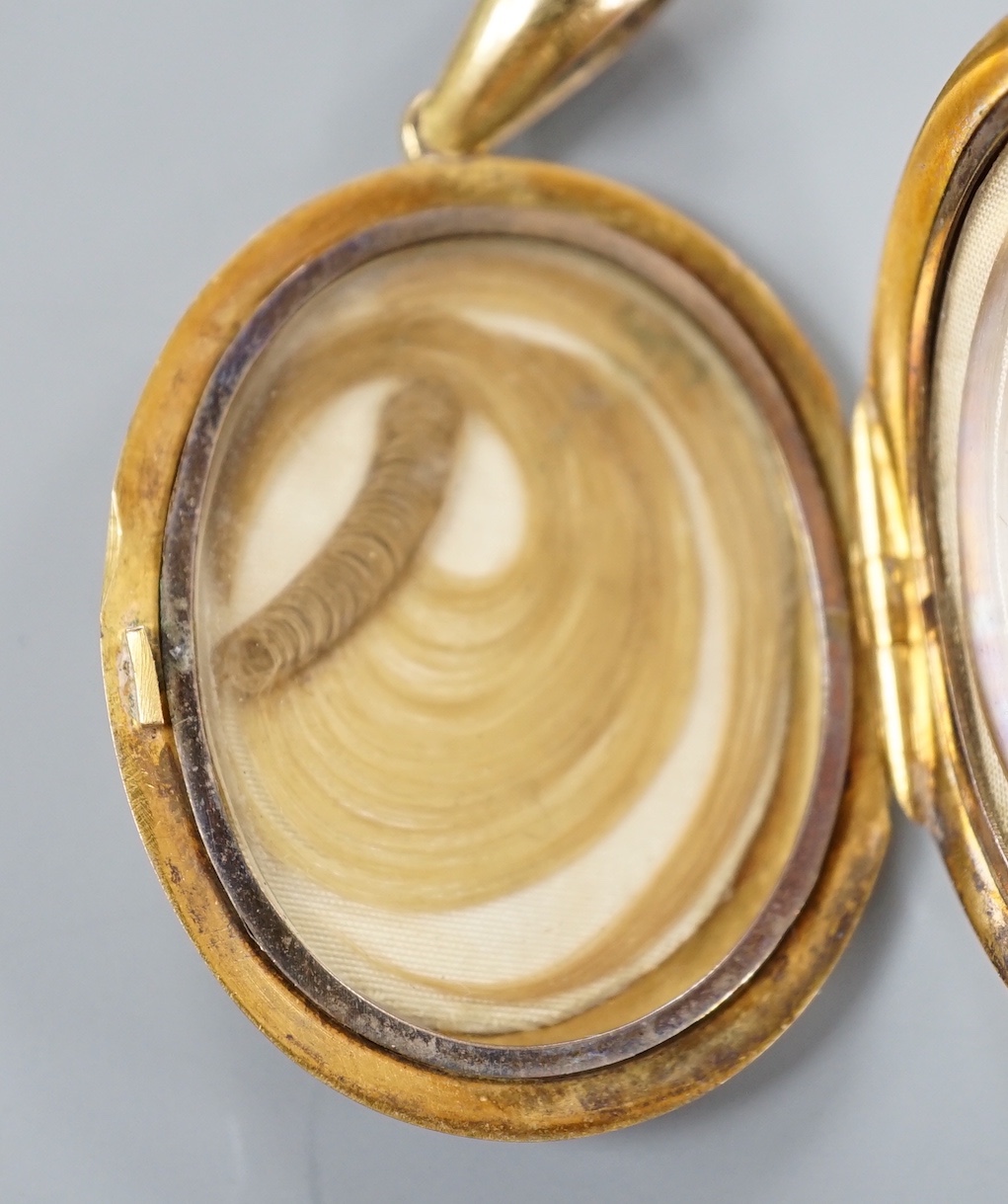 A late Victorian yellow metal oval mourning locket, containing plaited hair, overall 50mm, gross weight 14.7 grams.